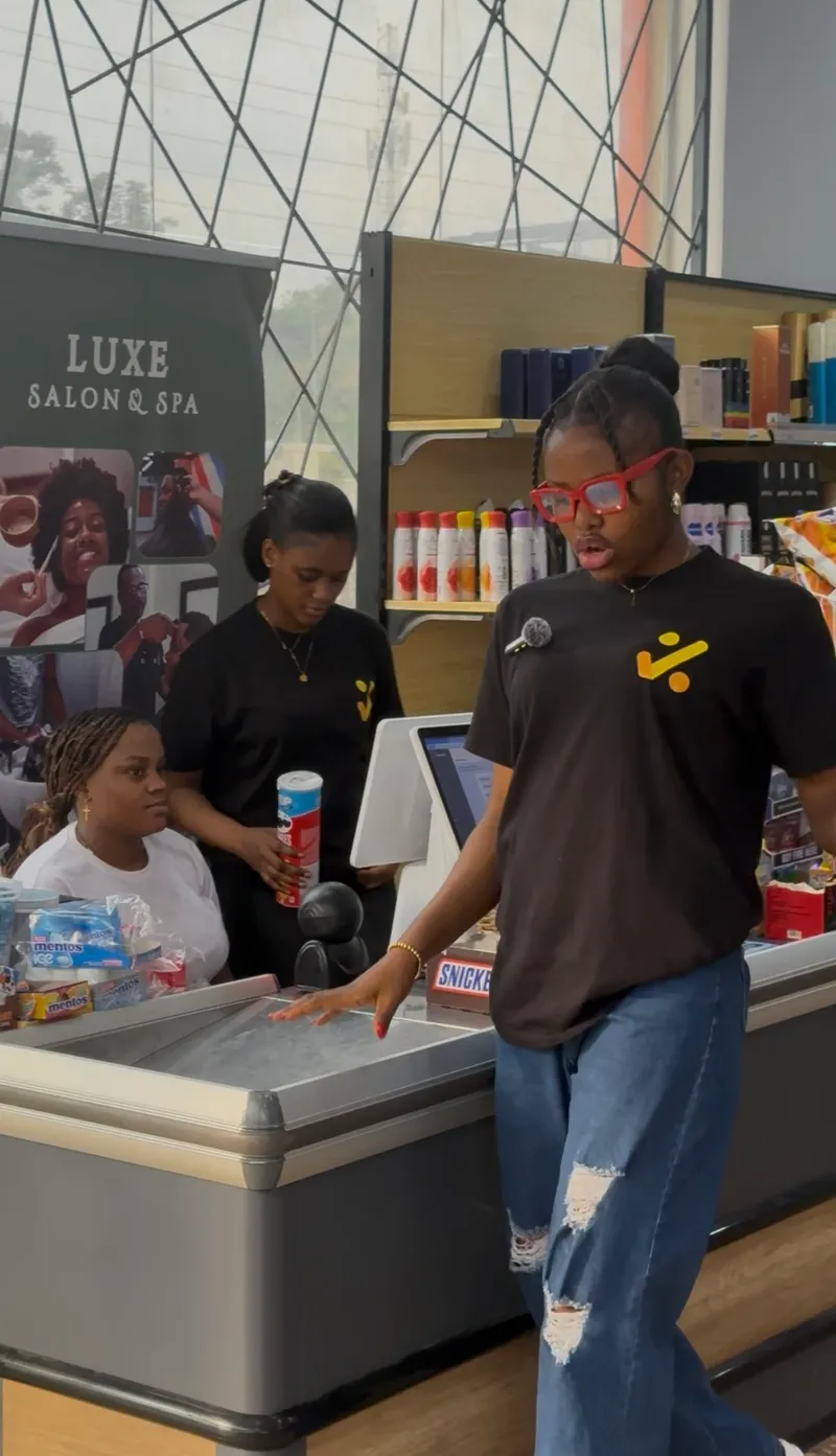 A Saletick trainer at a supermarket checkout counter with the cashiers and the point-of-sale screen behind her